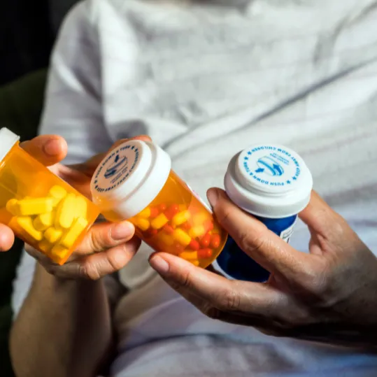 Person holding multiple medication bottles, representing psychiatric medication burden and risks from prescribing or dispensing errors.